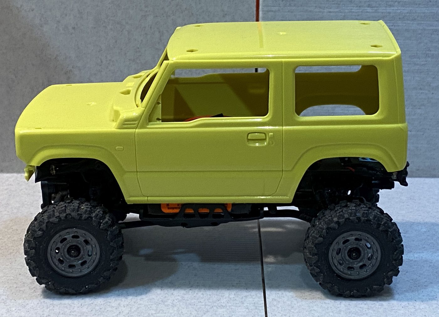 A yellow Suzuki Jimny body set on the chassis, wheels sitting close to correct within the arches.