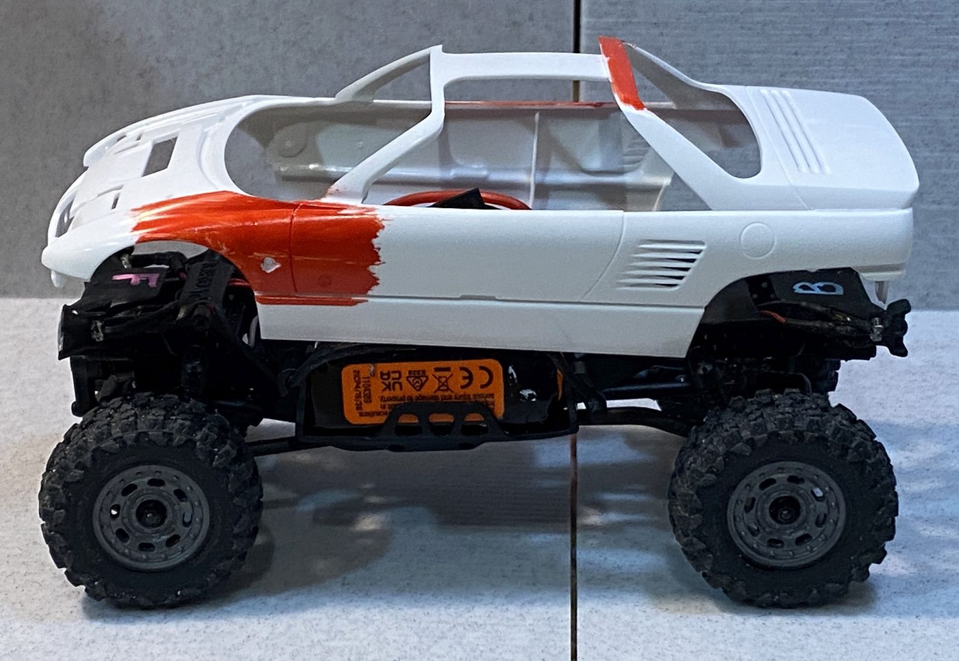 A white Mazdaspeed kei car body set on the chassis, small and shallow over the wheels.